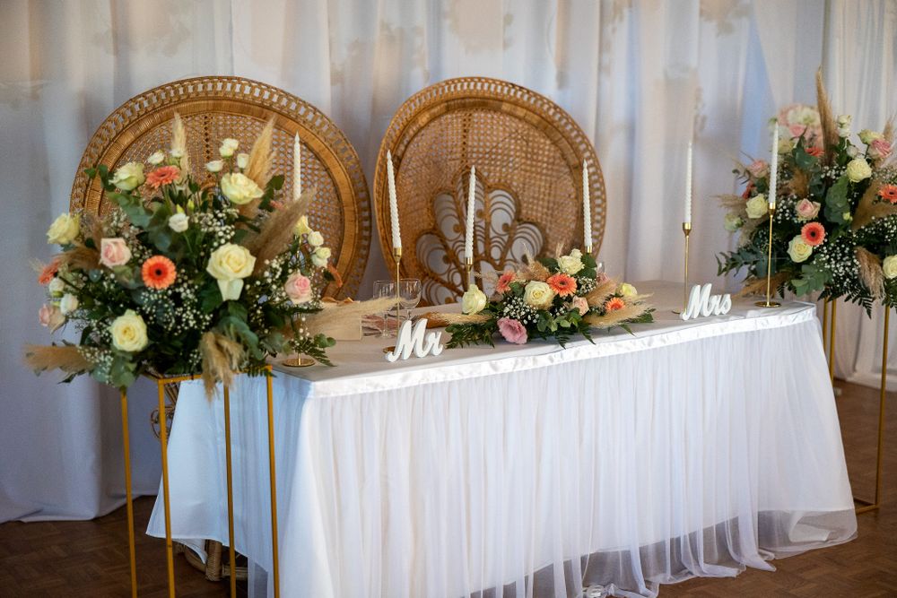 An elegant sweetheart table with peacock chairs and floral arrangements against white draping.