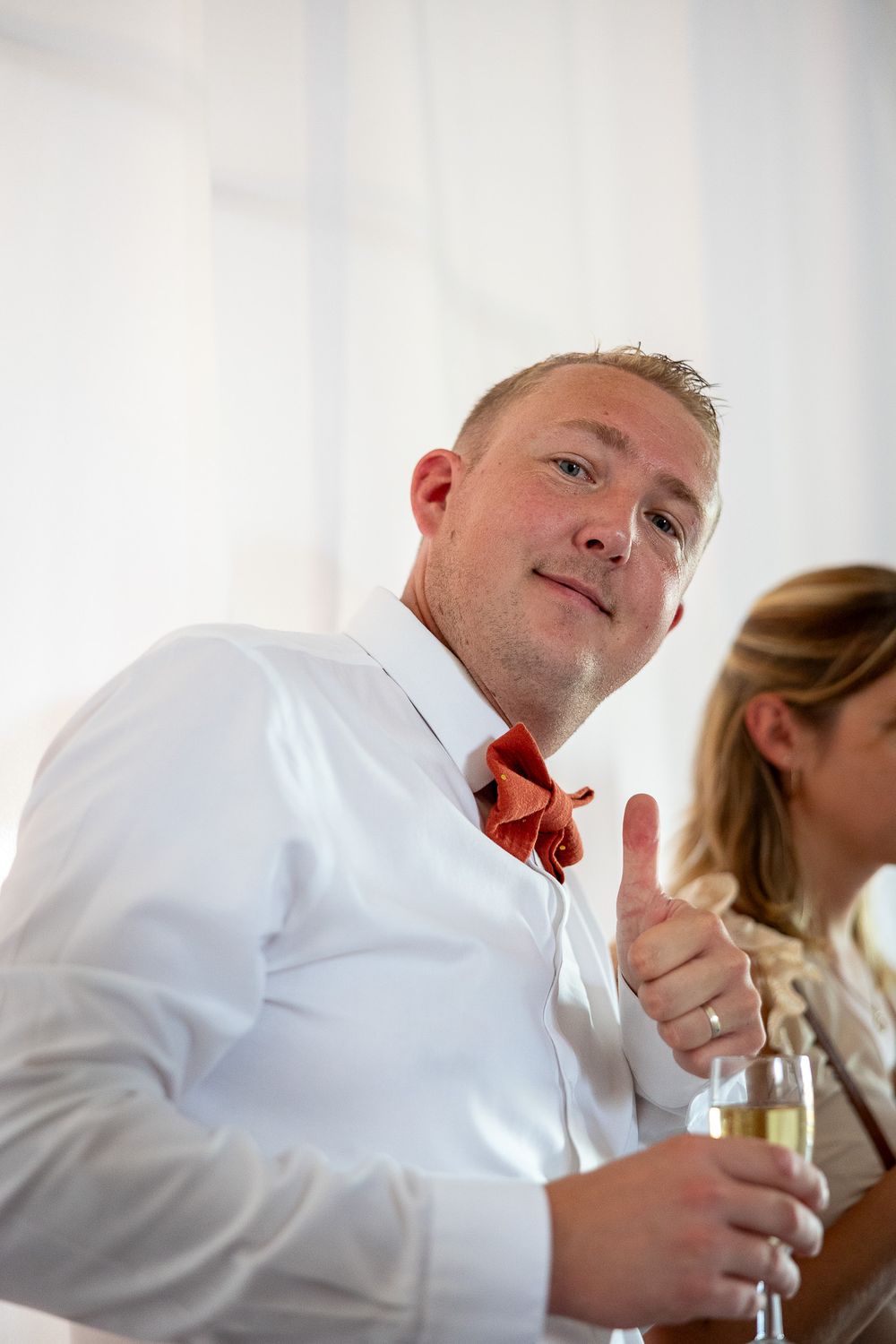 A guest in formal attire giving a thumbs up at a wedding reception.
