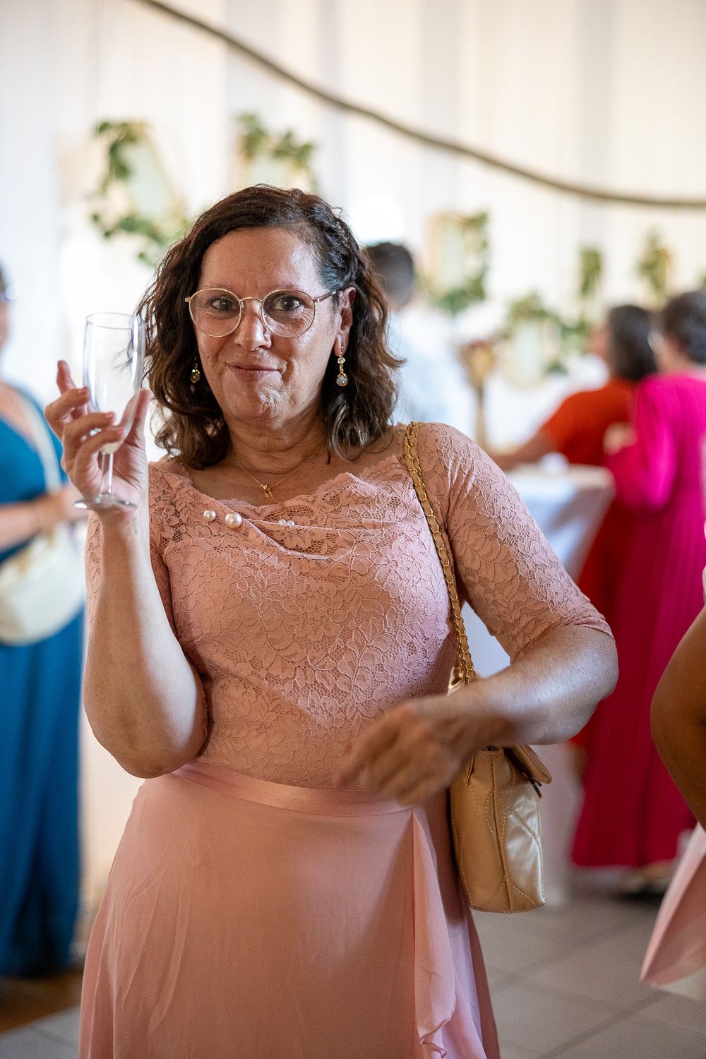 A wedding guest in a peach lace dress holding up a celebratory toast.