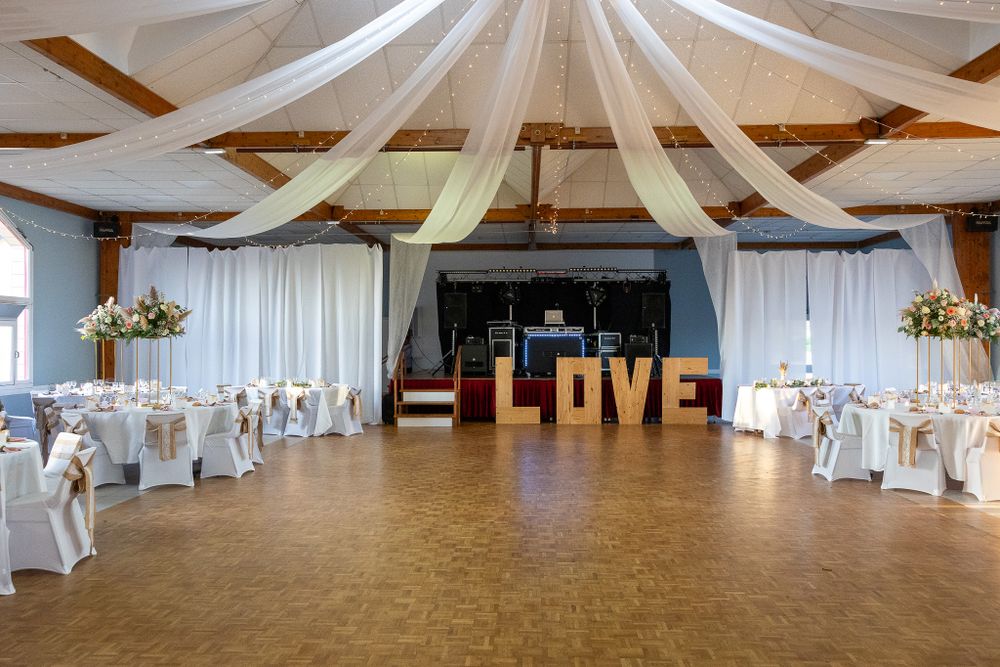 Wedding reception venue with elegant white fabric draping across ceiling and exposed wooden beams.