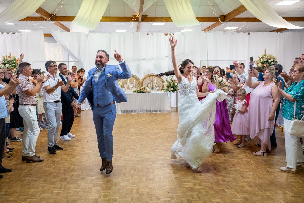 Wedding guests dancing and celebrating in a large reception hall with hardwood floors.