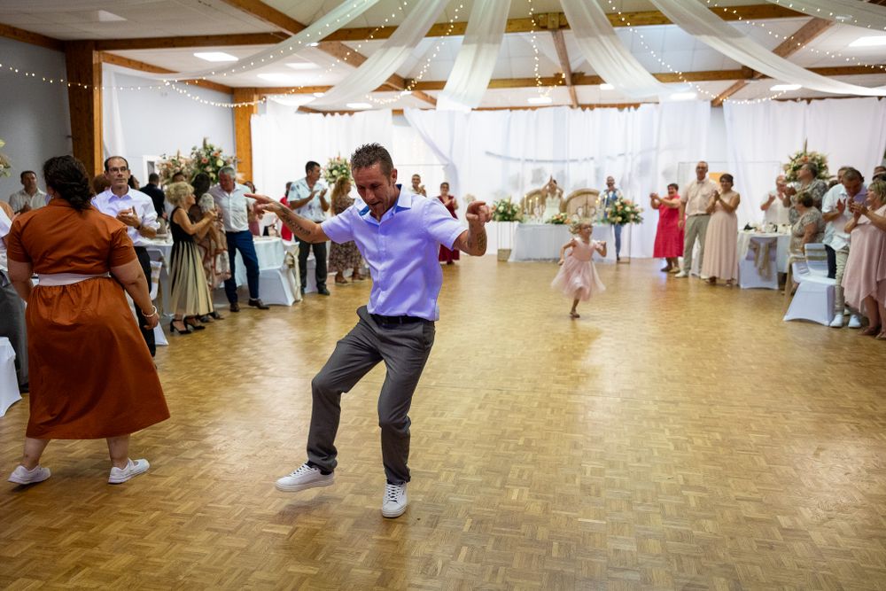 Wide angle view of wedding guests dancing in a reception hall with white draped decor.