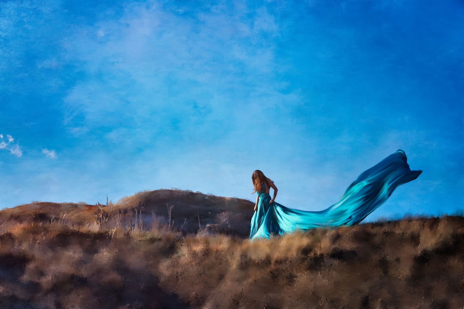 A flowing turquoise dress billows dramatically against a hilltop silhouette under a bright blue sky.