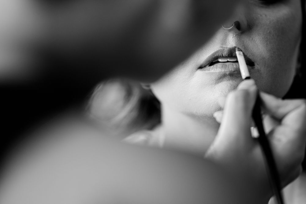 Black and white close-up photo of lips being touched up with makeup in soft focus.