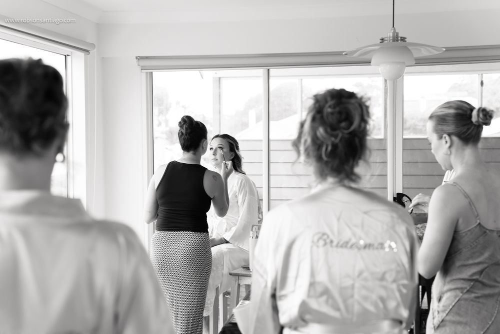 A black and white photograph showing people gathered in preparation for a wedding ceremony in a bright, sunlit room.