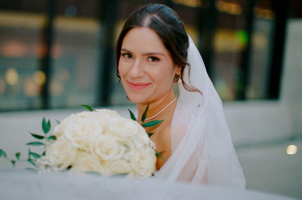A bride in a white veil holds a bouquet of white roses while smiling at her wedding at the Winter Park Events Center