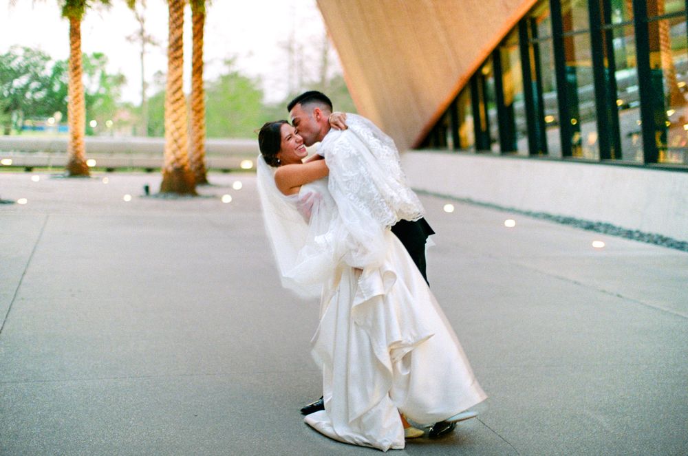 A romantic wedding moment captured outside a modern building with palm trees in the warm sunset light at the Winter Park Events Center
