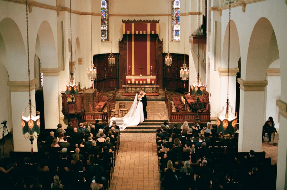 A photograph at Knowles Memorial Chapel wedding ceremony with guests seated in wooden pews and figures at the altar