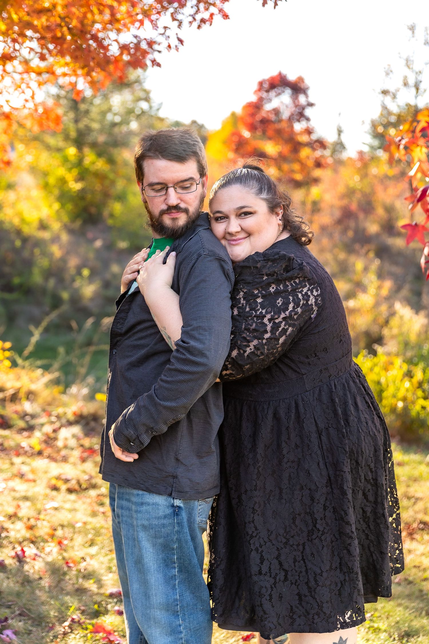 A couple embraces while posing for a portrait outdoors during autumn with vibrant orange and yellow fall foliage.