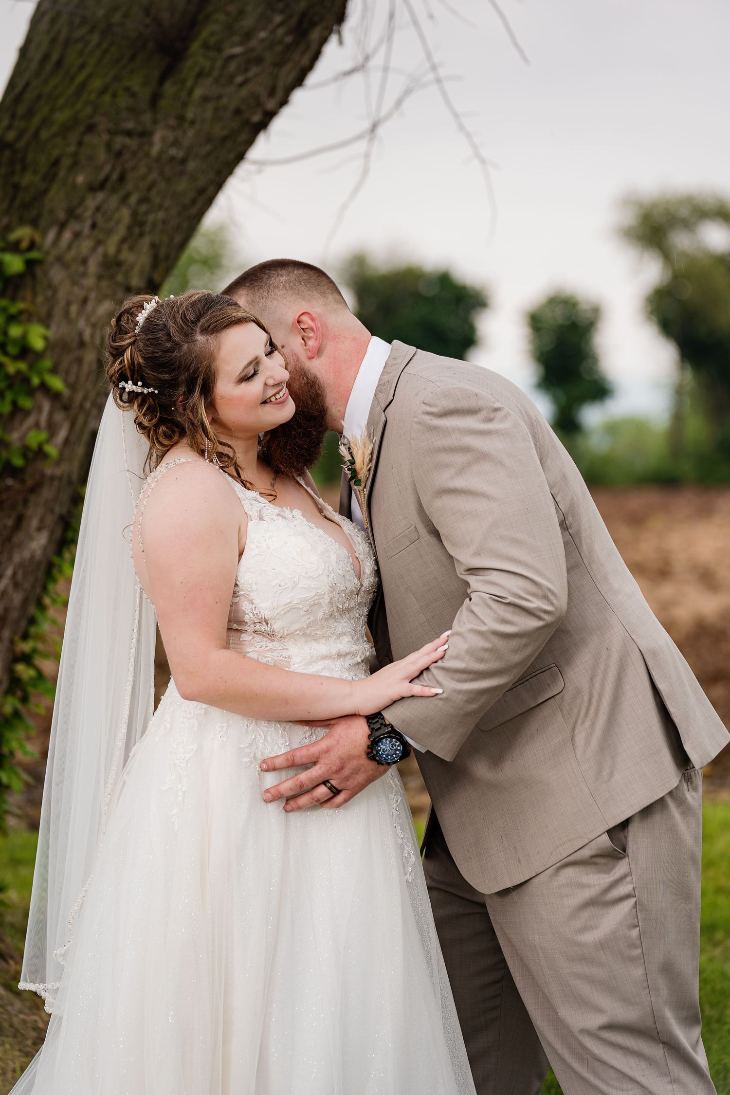 A tender wedding moment beneath a tree in a natural outdoor setting.