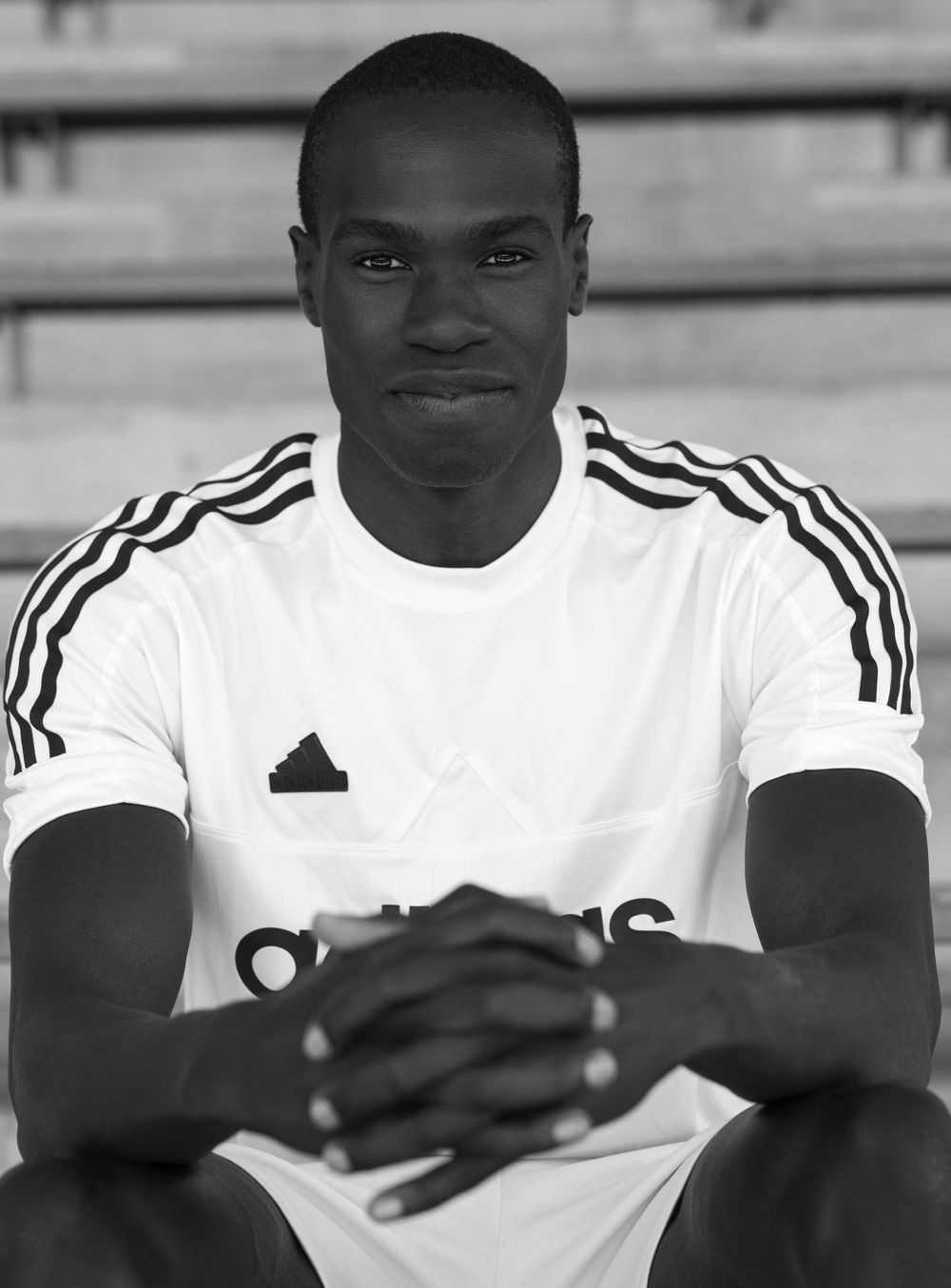 Athletic person wearing white Adidas jersey poses for portrait on bleachers.