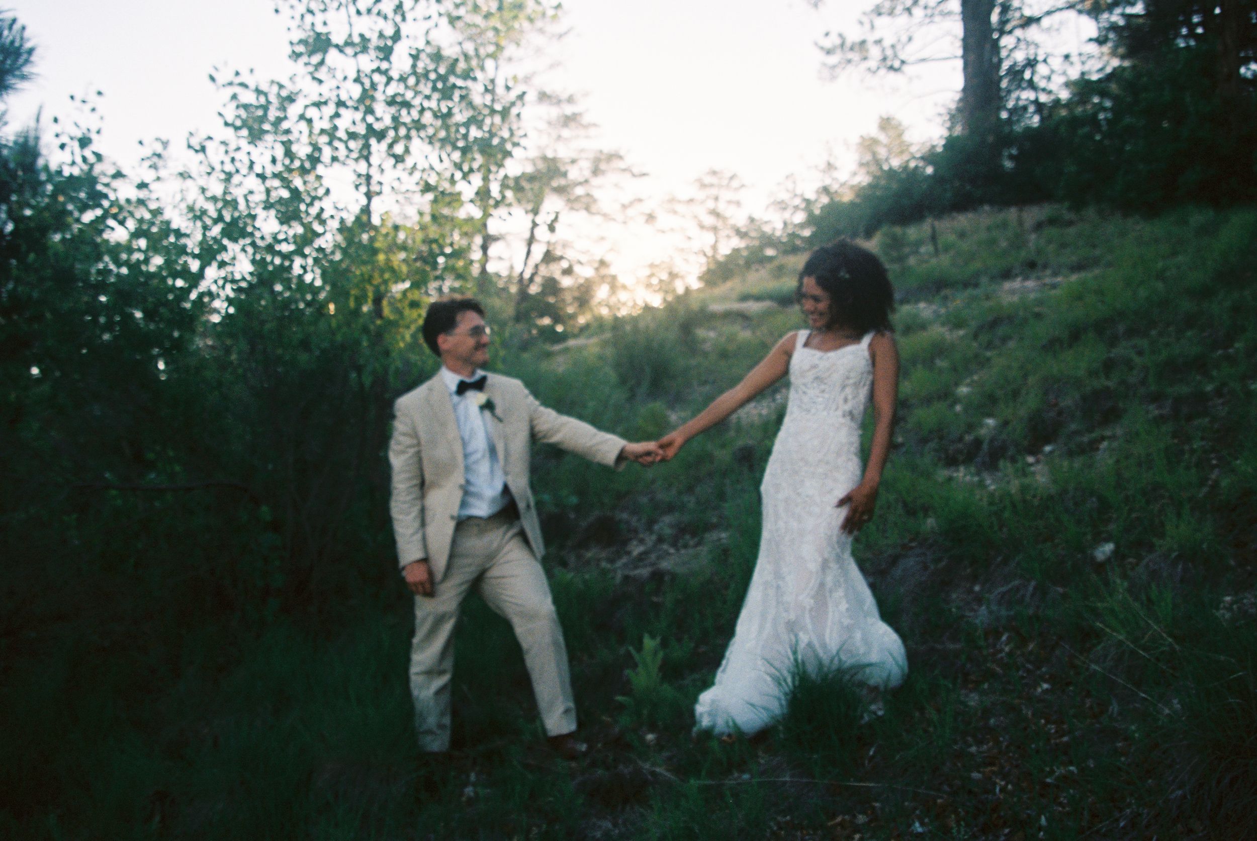 Happy couple walks hand in hand through a lush wooded trail during golden hour sunset.