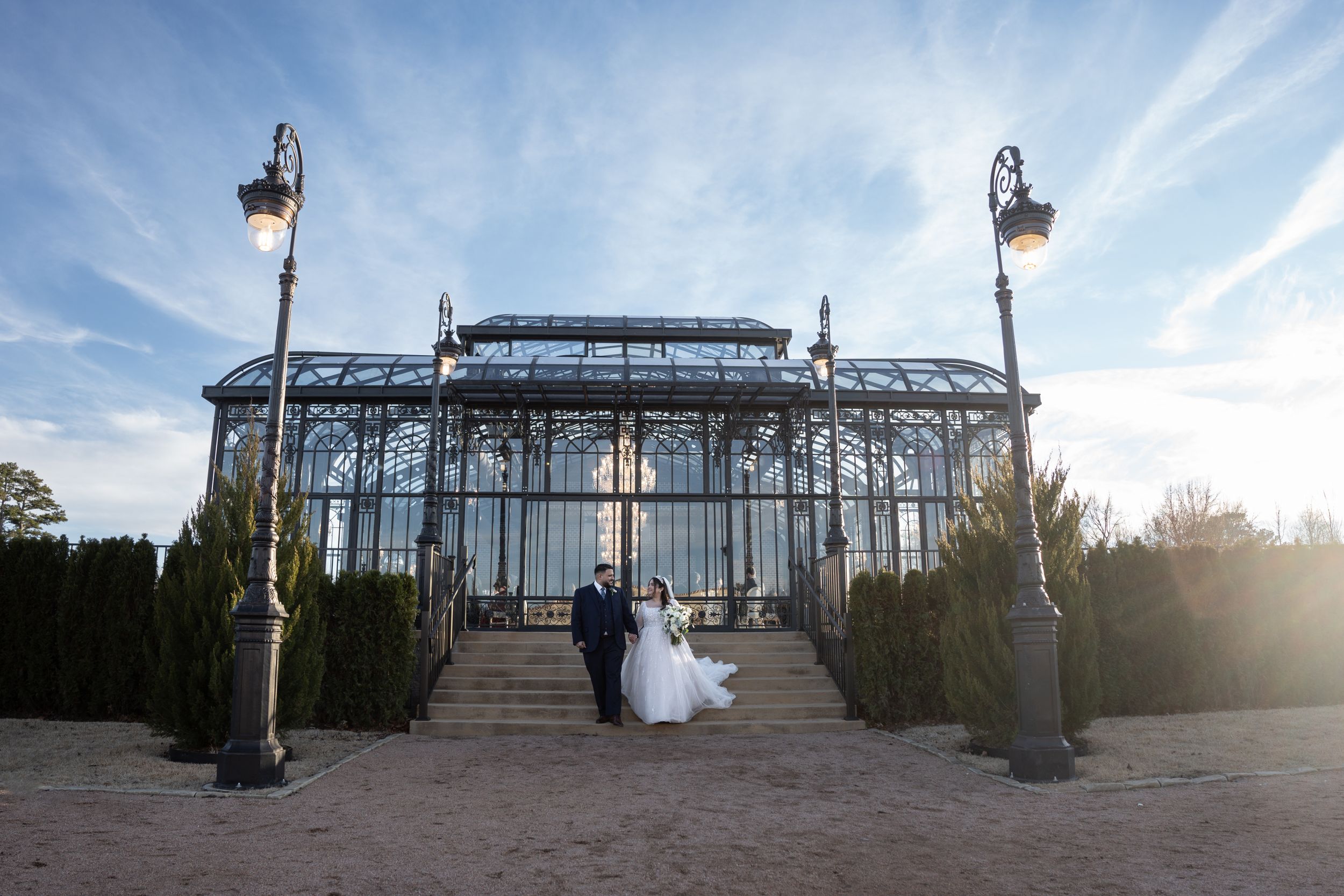 Silhouetted couple poses in front of grand glass conservatory building at sunset.