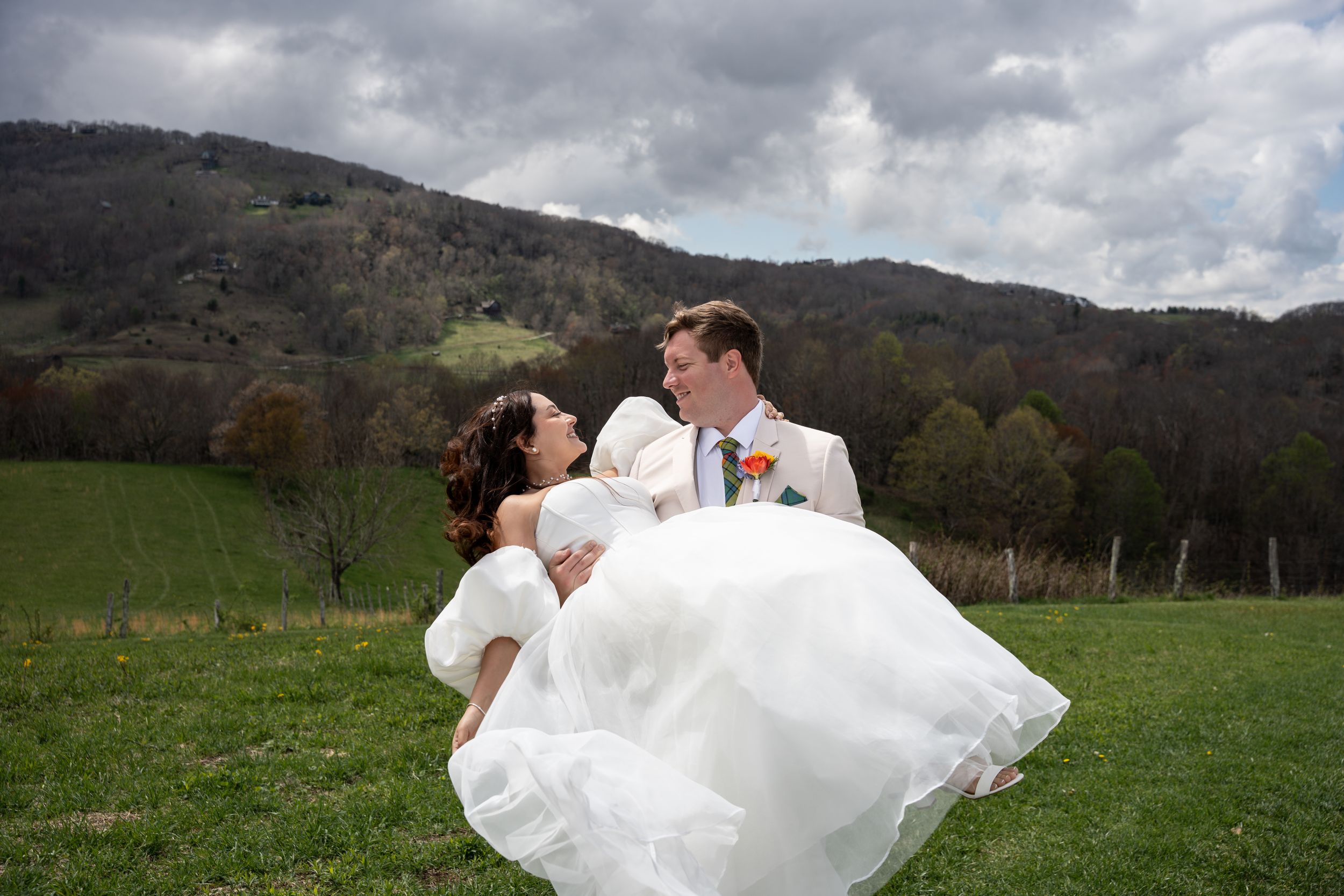 A romantic wedding couple embraces in a scenic mountain meadow on an overcast day.