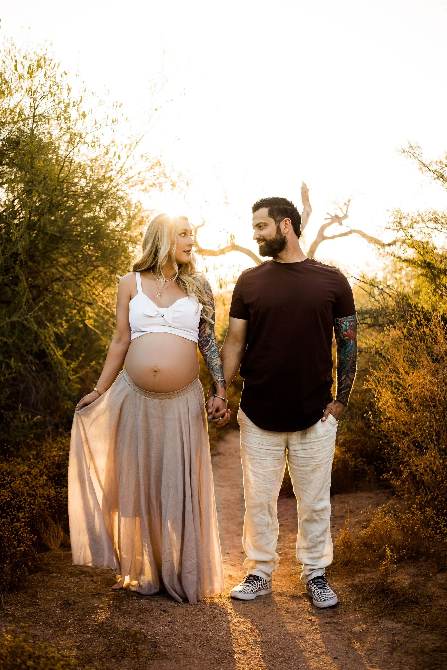 A golden desert glow maternity portrait of mom and dad holding hands and the mom to be has her dress flowing in the wind.