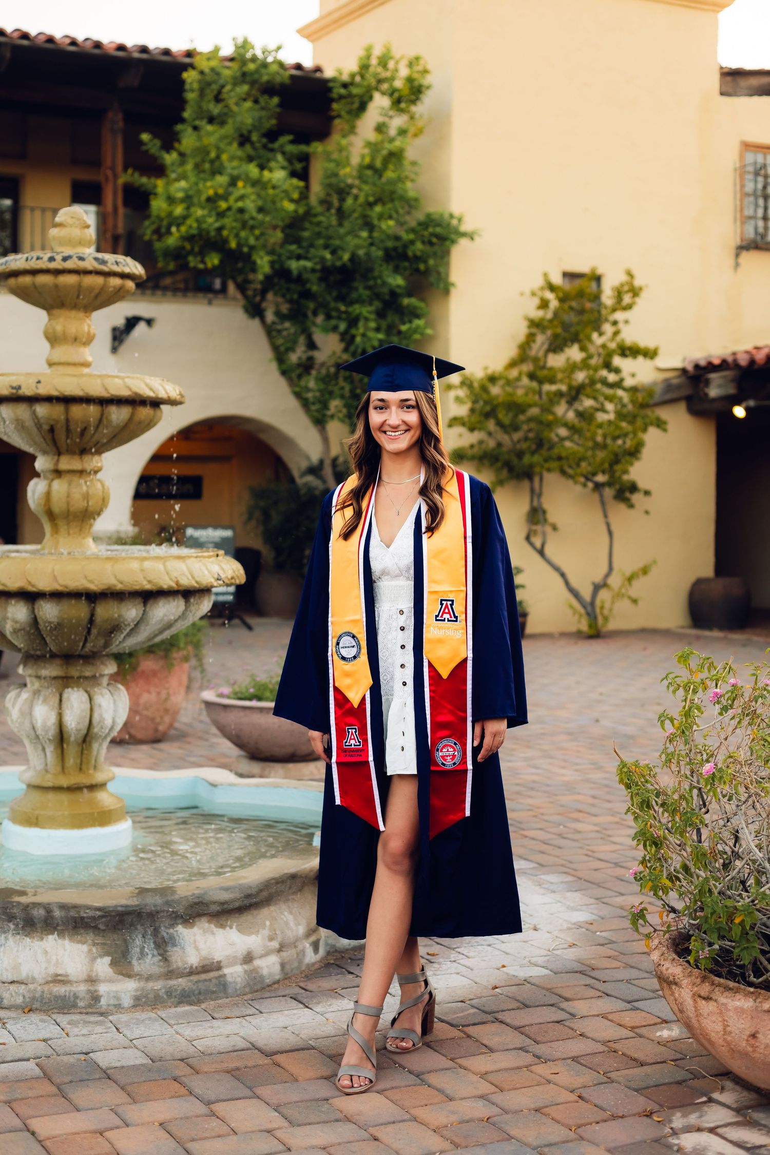 Senior graduate portrait of a girl wearing her college graduate cap and gown next to a water fountain in Arizona.
