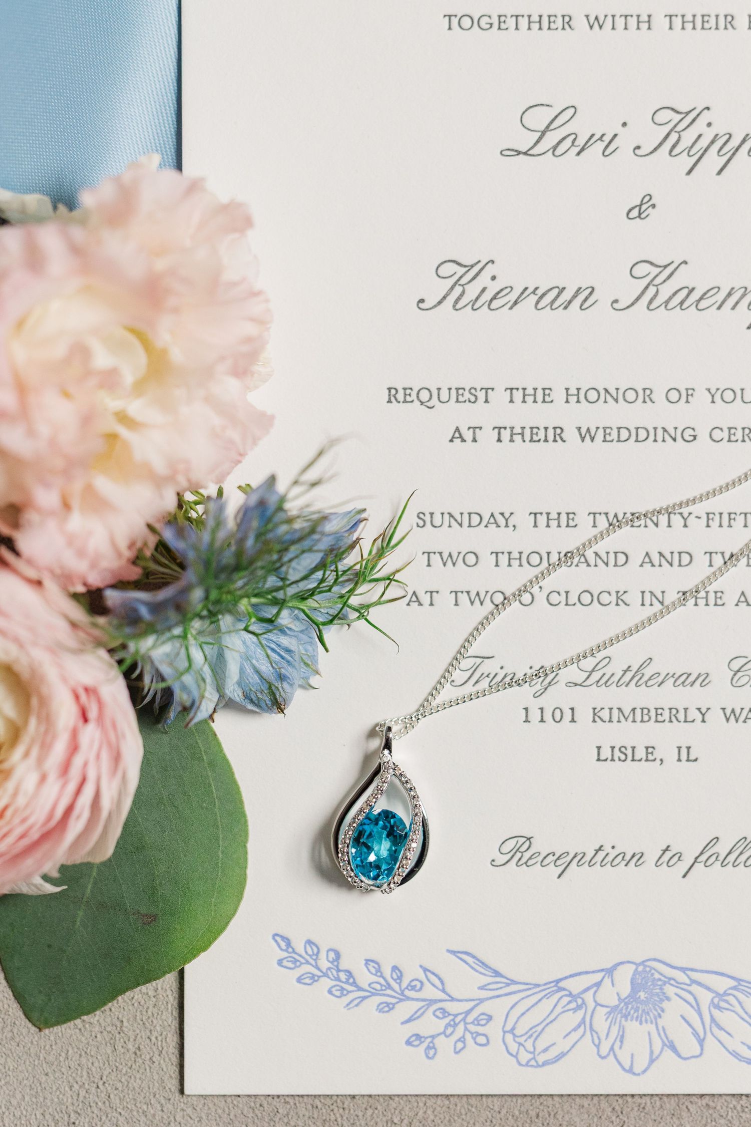 Wedding invitation details with elegant calligraphy, pink flowers, and blue decorative accents on white paper.