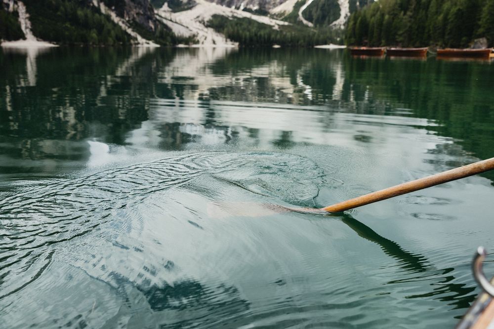 Kayakers paddle across a serene mountain lake surrounded by snow-capped peaks and misty evergreen forests.