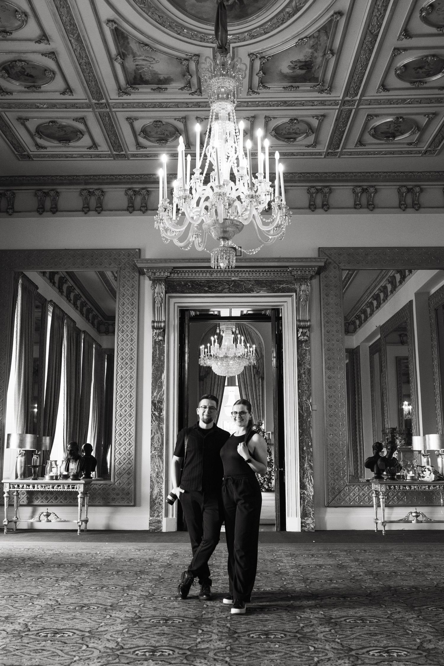 Grand ballroom with ornate ceiling, crystal chandeliers, and mirrored walls captured in black and white.