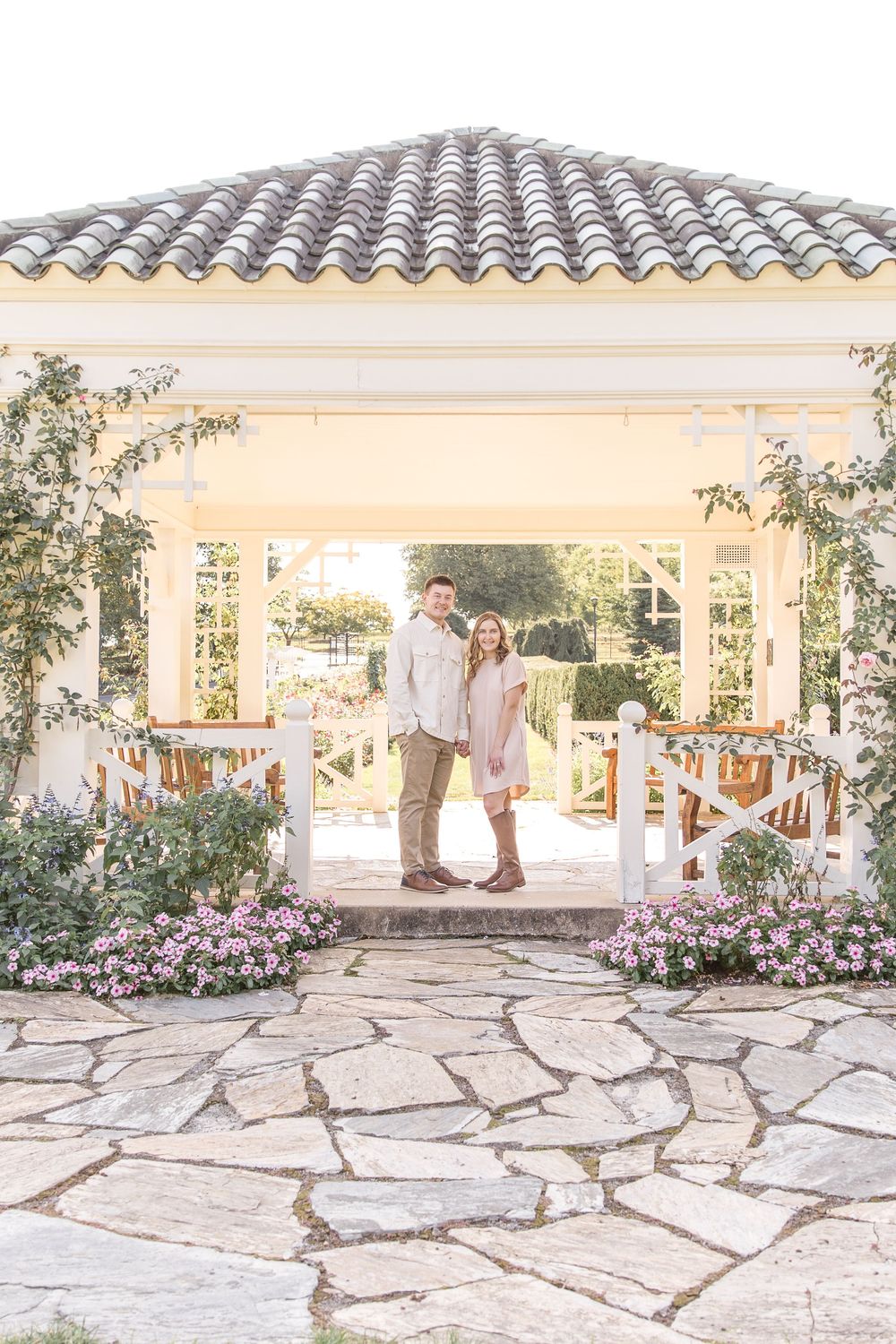 Beautiful garden gazebo with stone patio floor, pink flowers, and elegant tiles roof creates romantic outdoor setting.