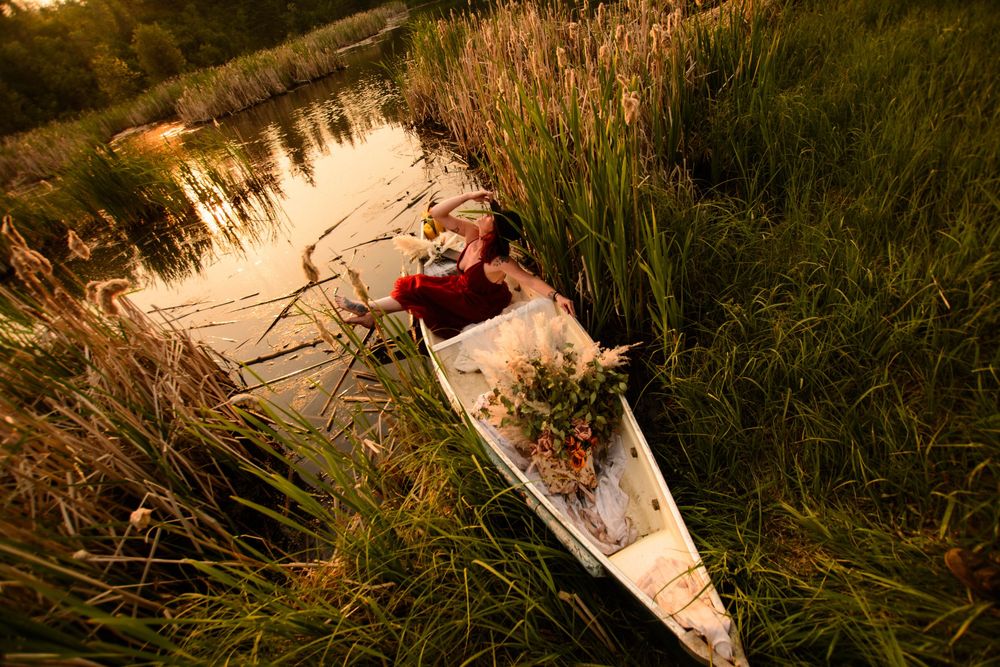 A person lying among flowers in tall grass during sunset creating a dreamy outdoor portrait.