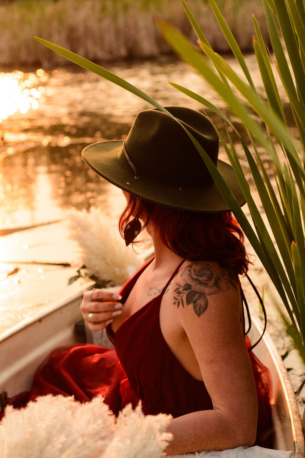 A person in a wide-brimmed hat and red dress relaxes by the water during golden hour, with palm fronds in view.