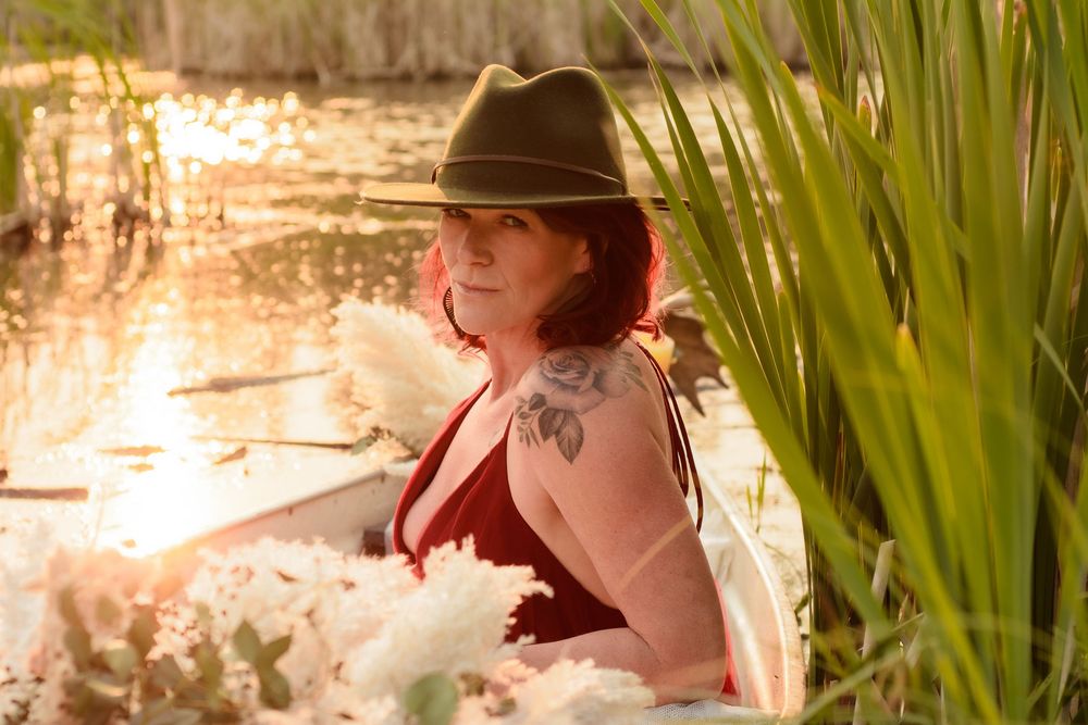 Person in a sun hat walking through a lush garden path with tall grasses and flowering plants.