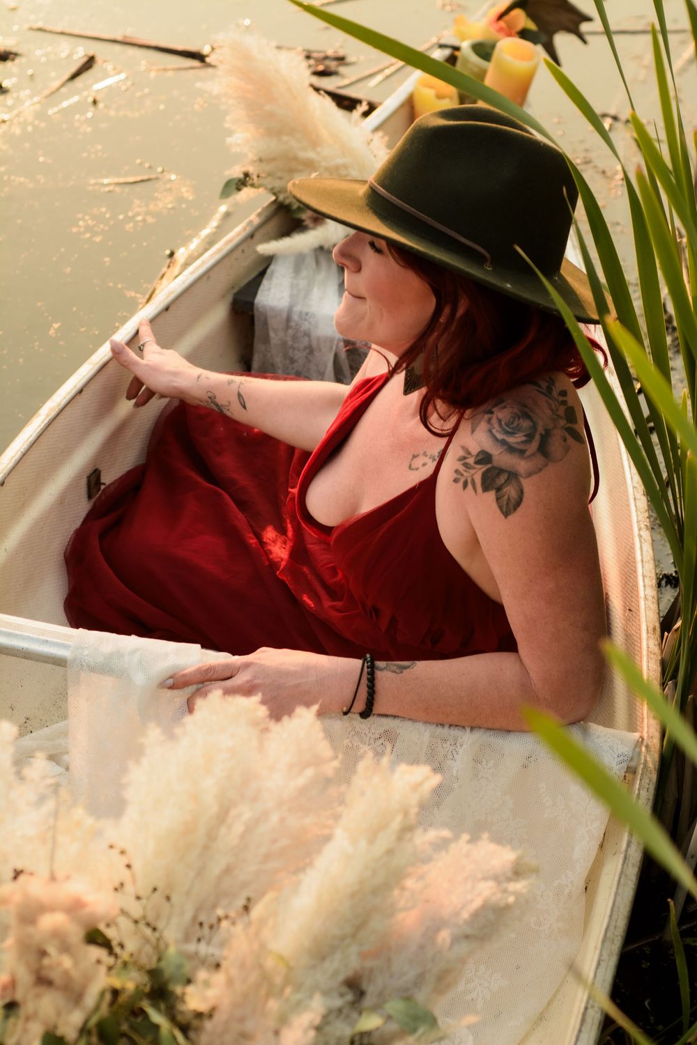 A figure in red and a safari hat rests in a vintage white bathtub outdoors among tropical plants.