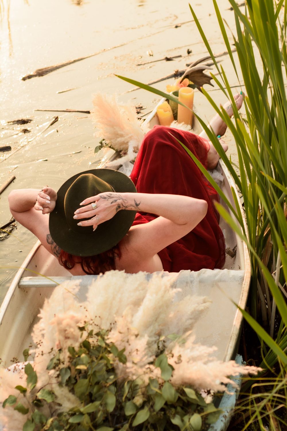 A relaxed person lounging in a small boat surrounded by tall reeds and ornamental grasses on a sunny day.