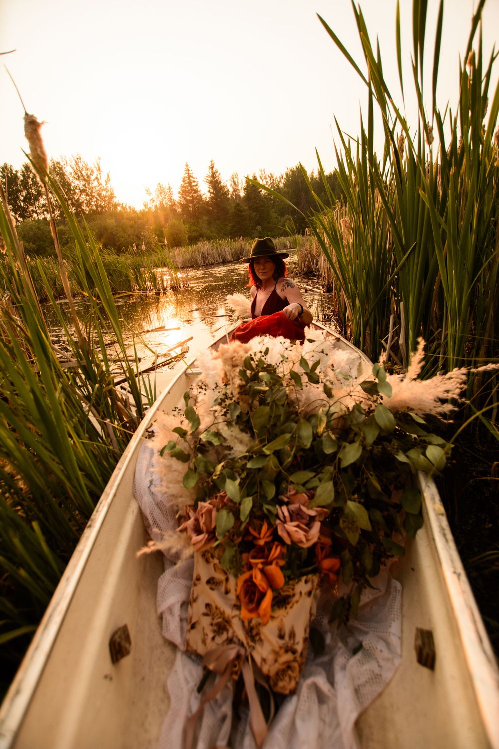 Ethereal sunset scene with a small boat decorated in autumn foliage gliding across tranquil waters amid tall reeds.