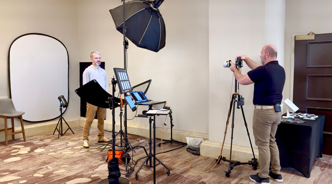 Professional photo studio setup showing photographer capturing headshots with lighting equipment and reflector screen.