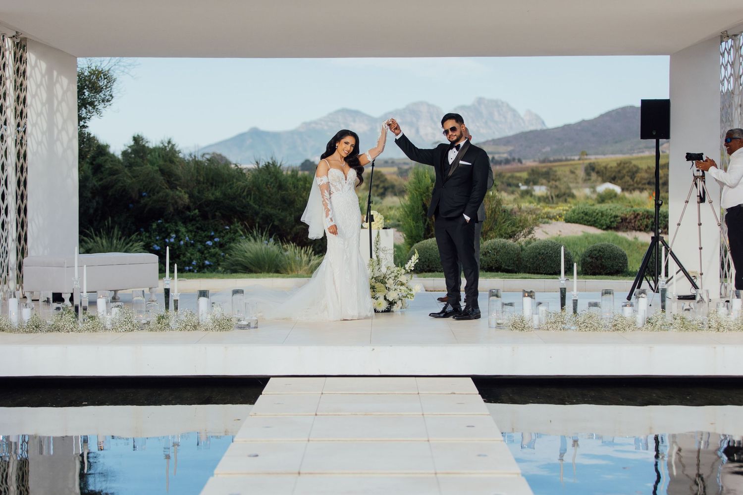 Wedding couple celebrates on an outdoor venue stage with mountains and pool in view at a luxury destination wedding.