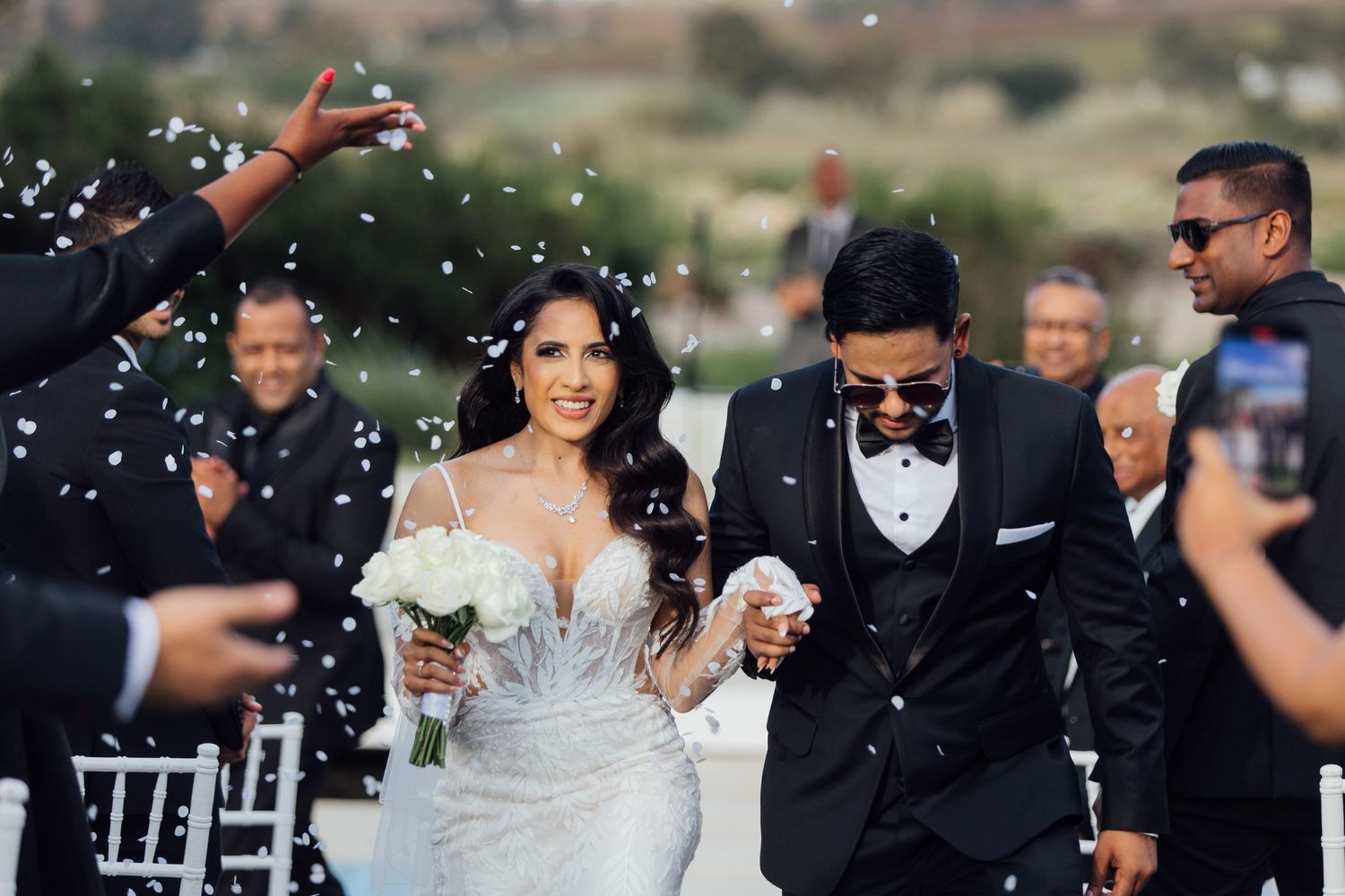 Wedding guests celebrate with confetti as the newlyweds exit their outdoor ceremony.