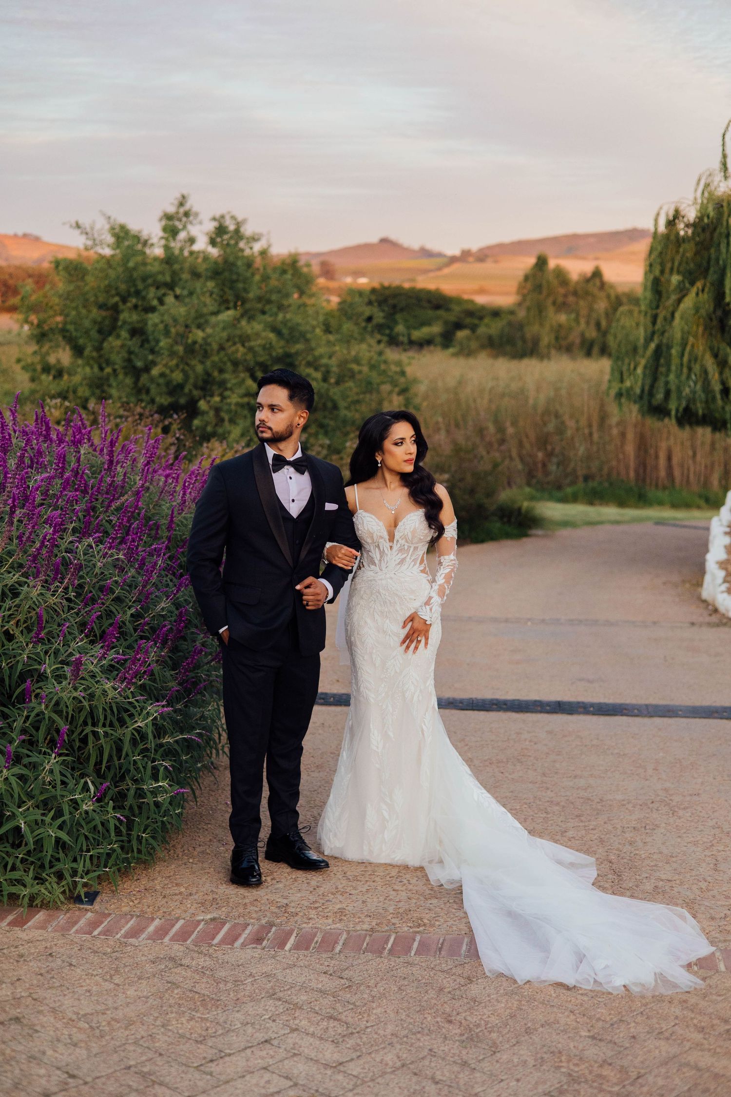 A romantic wedding photo series against the winelands mountains with purple wildflowers and sunset lighting.
