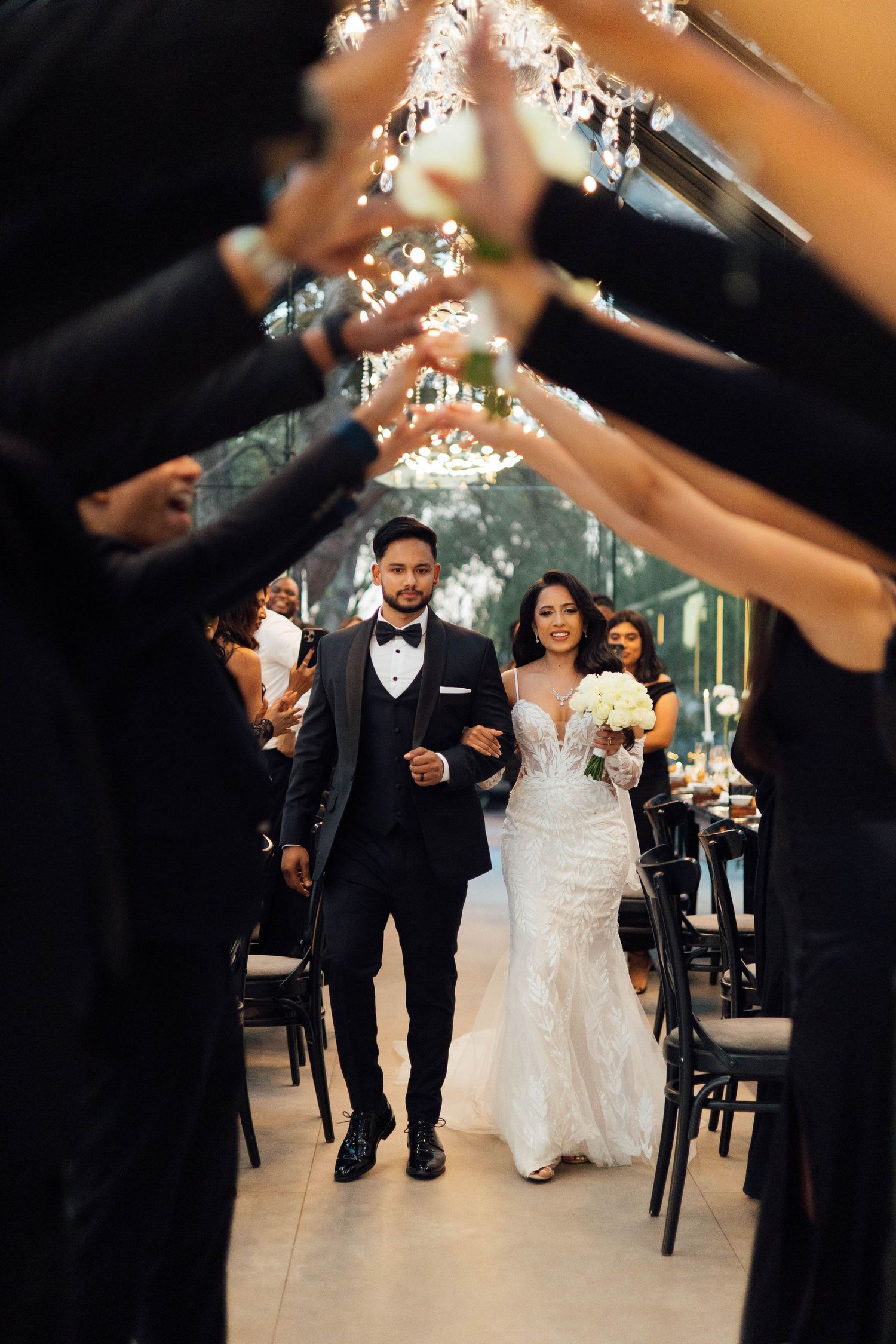 Newlyweds enters their reception while wedding guests create archway with raised arms