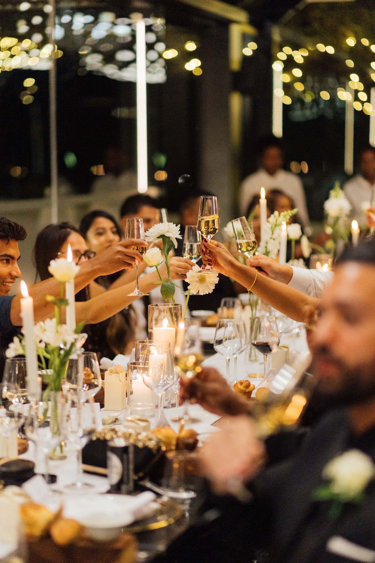 Dinner guests raise wine glasses for a festive toast at an elegant candlelit table decorated with floral centerpieces.