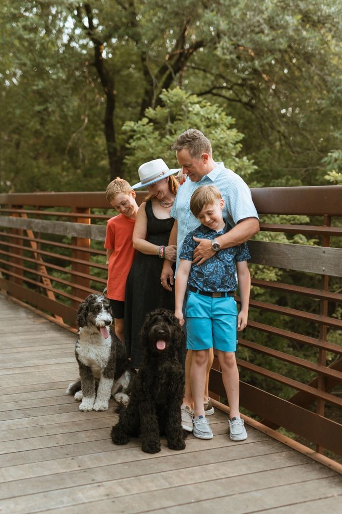 Group poses with two large dogs on a wooden bridge surrounded by lush greenery.