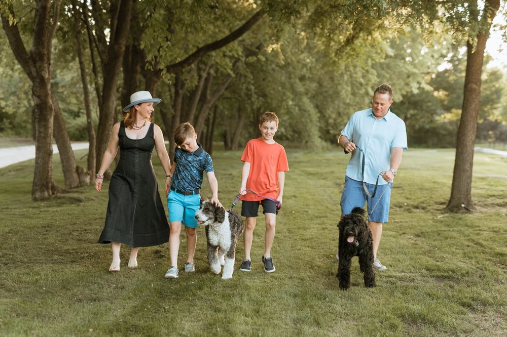 A group walks together with their black dog on a tree-lined path during a summer evening.