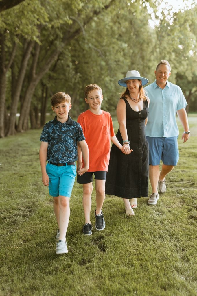 A family of four walks together on a grassy path lined with trees during golden hour.