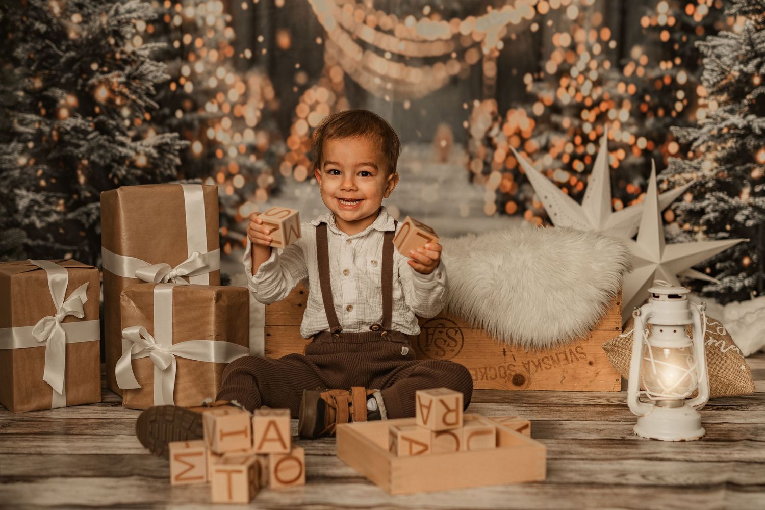 Vintage holiday portrait of a child in suspenders playing with wooden blocks among Christmas decorations.