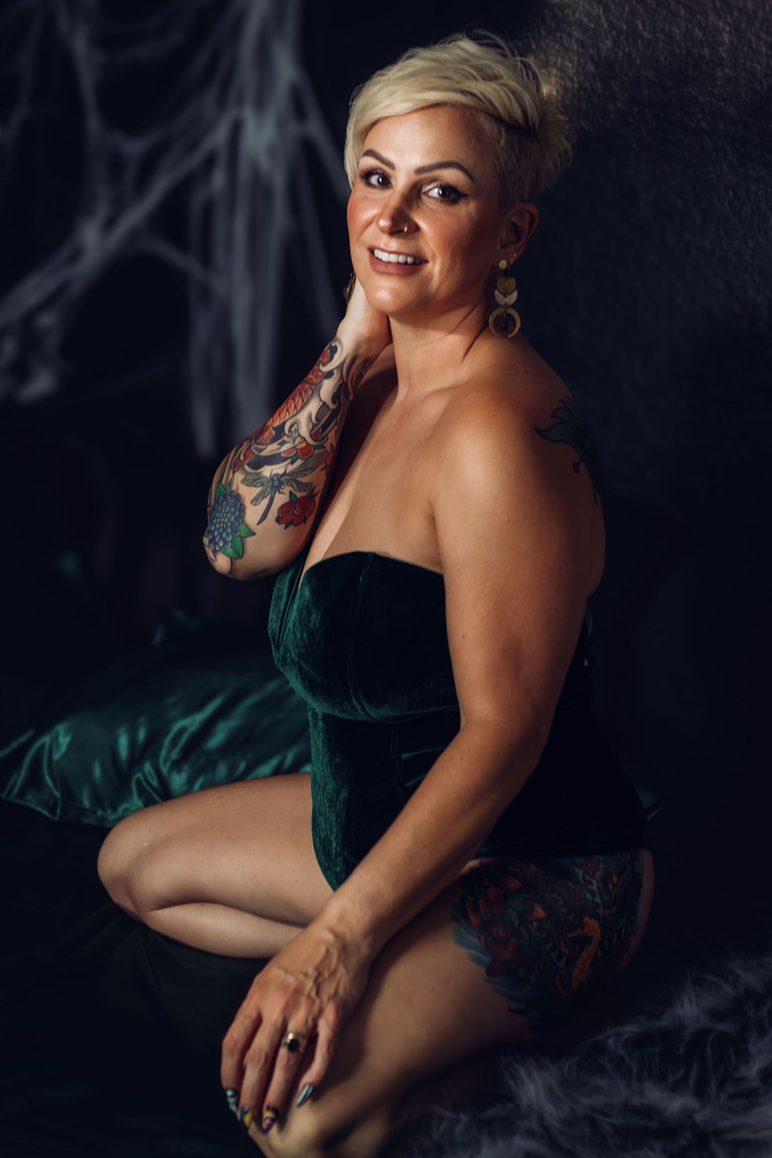 Client in emerald velvet bodysuit during Fort Worth boudoir session, smiling confidently in moody studio lighting.
