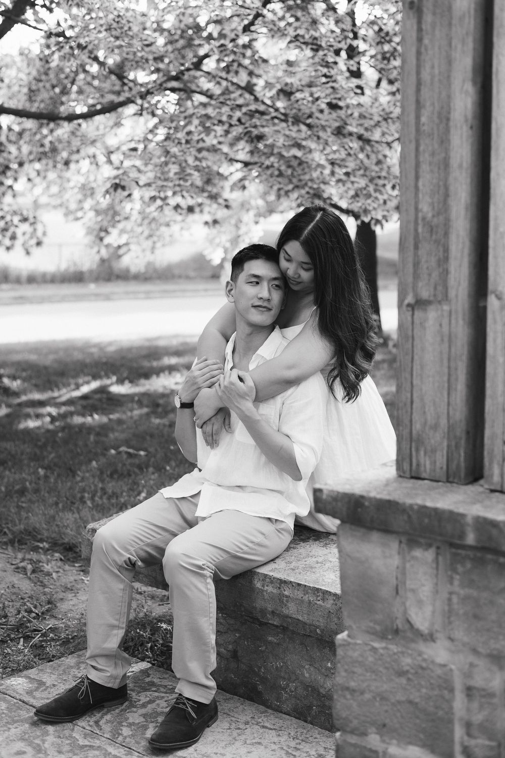 Black and white photo series showing romantic couple embracing on stone steps outdoors under trees on a sunny day at Rockway Gardens