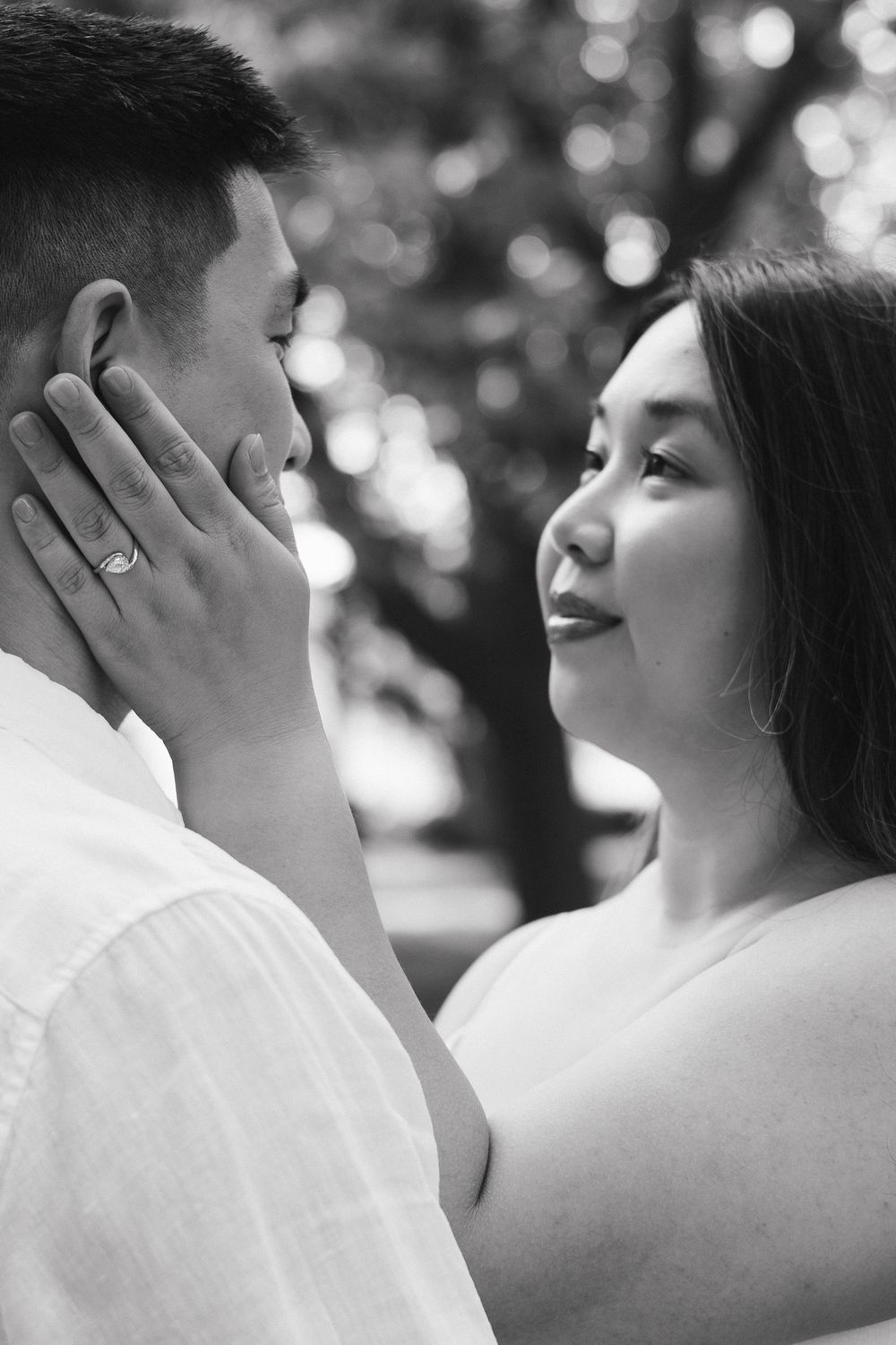 Intimate black and white portrait of a couple in white clothing sharing a tender moment outdoors with bokeh background at Rockway Gardens