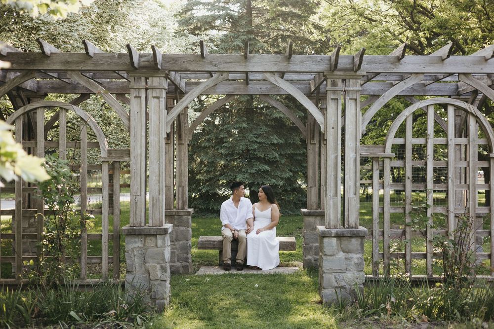 A romantic scene under a weathered stone garden pergola with climbing vines and greenery in a serene outdoor setting at Rockway Gardens