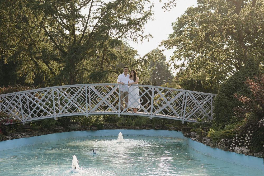 A person kneels beside a small decorative fountain in a tranquil garden setting surrounded by lush greenery at Rockway Gardens in Kitchener