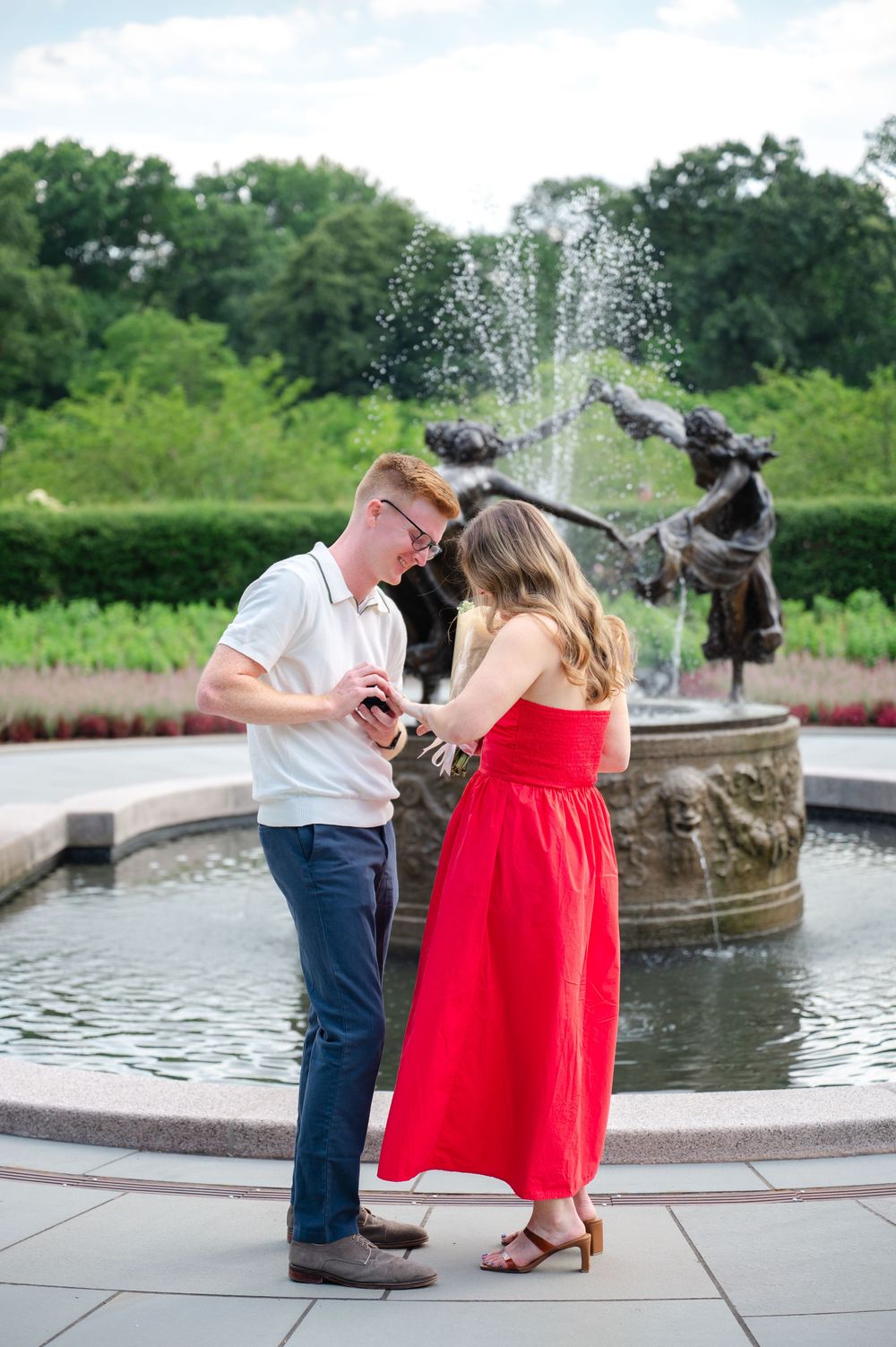 A couple shares a romantic surprise proposal moment by an ornate fountain in the Conservatory Gardens of Central Park.
