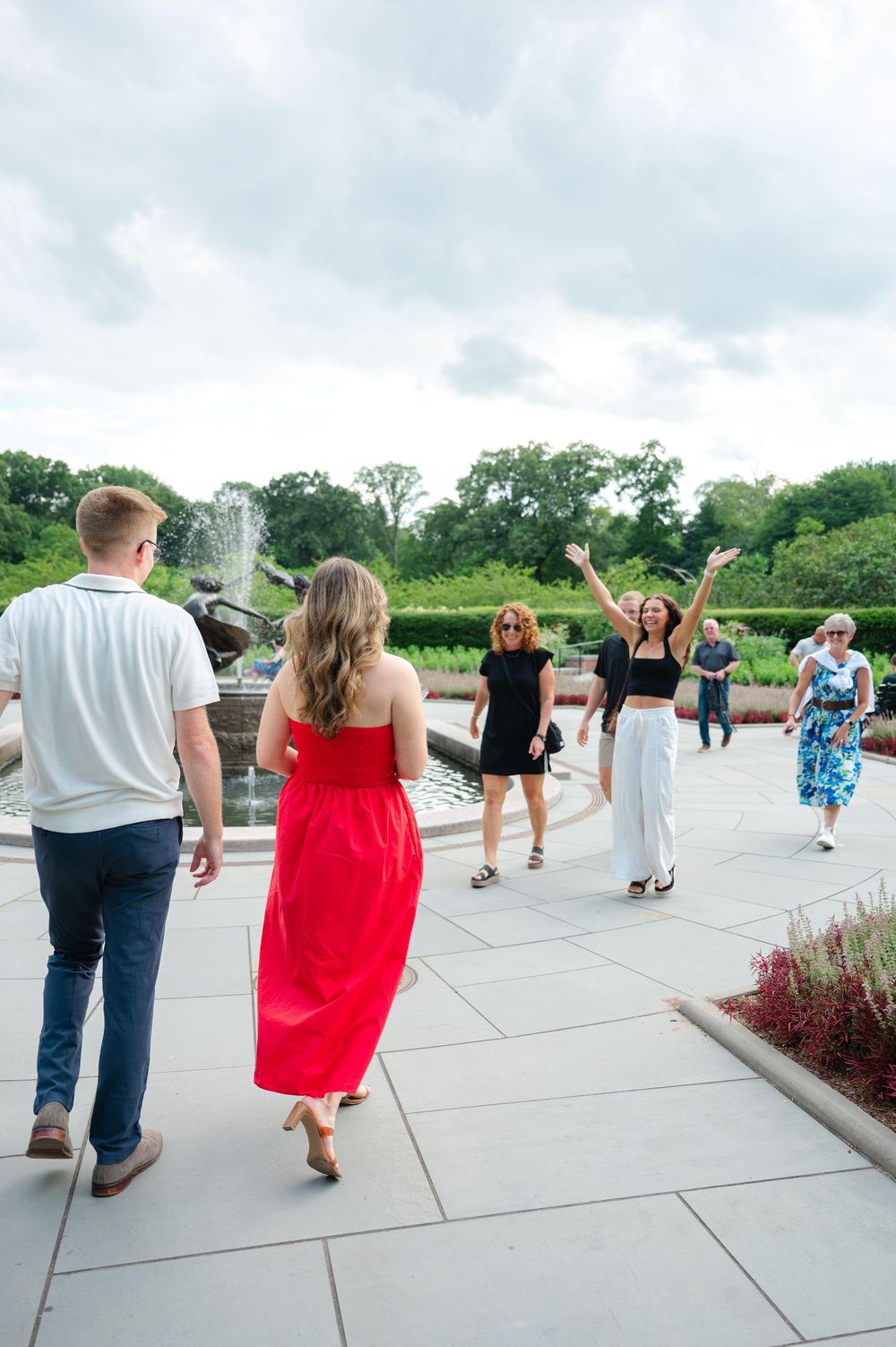 A group of people celebrating a couple's engagement in the Conservatory Gardens of Central Park in front of a fountain.