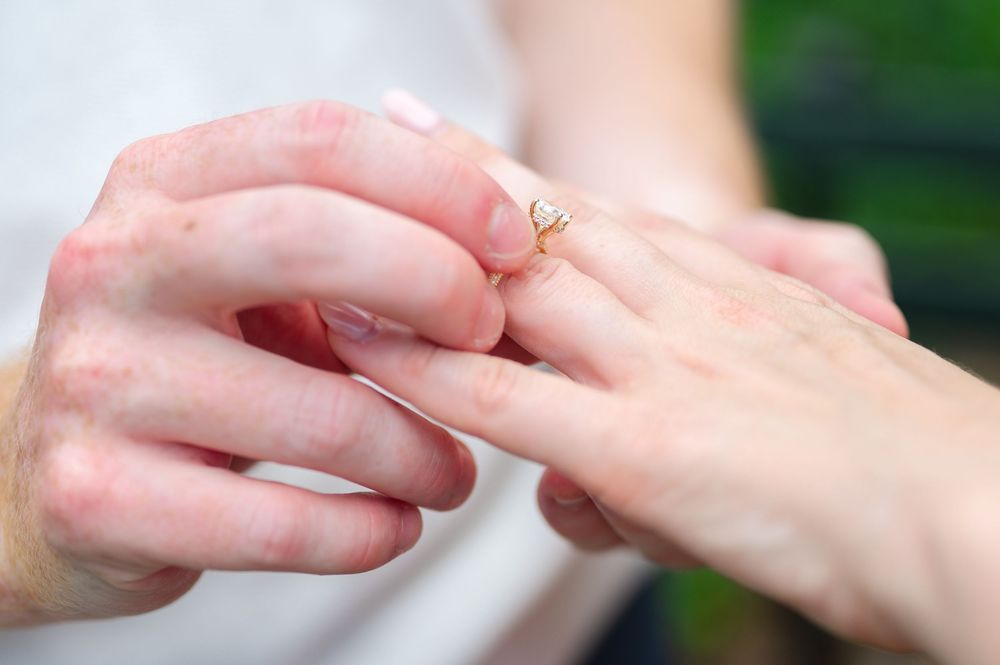 A man slides an engagement ring on a woman's finger during a proposal moment captured by best NYC proposal photographer.