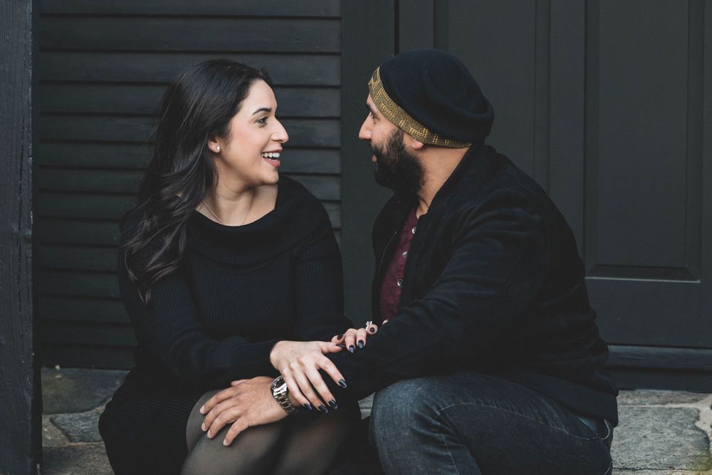 A couple laughs together while sitting outdoors during a candid engagement photo session.