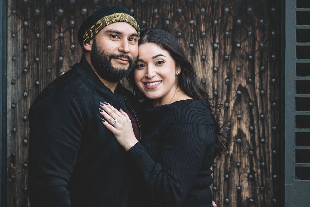 A couple embraces in front of a textured wooden door during their engagement session.